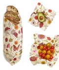 Bread, a sliced avocado, and tomatoes each wrapped with Bee's Wrap.