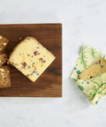 Bread and a cheese sandwich on a cutting board, and another cheese sandwich wrapped in Bee's Wrap.