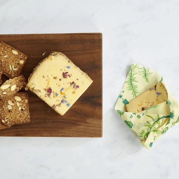 Bread and a cheese sandwich on a cutting board, and another cheese sandwich wrapped in Bee's Wrap.